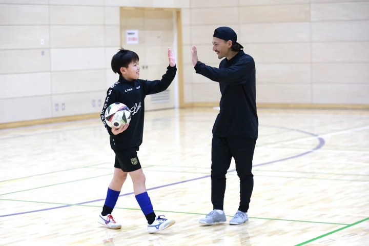 体育館でボールを持つ子どもとハイタッチをする石関聖